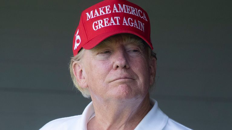 Donald Trump i vit golfskjorta och röd Make America Great Again-keps.