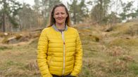 En person (Annika Kolster) med gul ytterjacka står utomhus i en skogsmiljö.