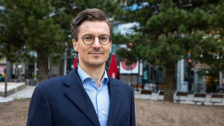 Mies seisoo puistomaisessa kaupunkiympäristössä.
