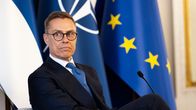 President Alexander Stubb sitting in a chair, with EU, Nato and Finnish flags in the background.