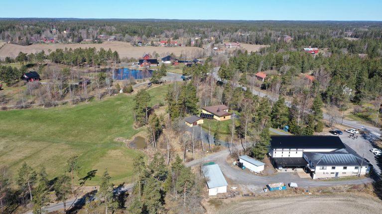 En flygbild över en golfbana, åkrar och hus då våren börjar grönska i träden.