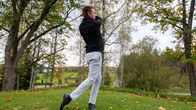 Mies tekee syksyisellä golf kentällä golfswingin mailalla.