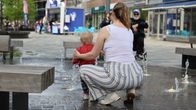 Mother and a toddler cooling off at a street fountain on a hot day.