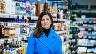 Emma Kajander i blå jacka framför en massa alkoholflaskor i en butik.