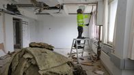 En byggarbetare står halvvägs på en stege och fixar med något i taket. 