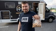 Kultakauppias Matias Kerminen pitää kädessään läpinäkyvää muovipussia, jossa kultaisia rannekoruja ja sormuksia. Taustalla mainostekstein teipattu asuntoauto. 