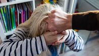 Miehen käsi tukistaa vaaleahiuksisen tytön hiuksia ja tyttö yrittää pyristäytyä irti.