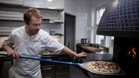 Restaurangägare Nick Victorzon skyfflar in en pizza i ugnen.