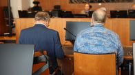 Oikeudenkäynnissä syytetyn ja puolustusasianajajan selät, taustalla oikeuden henkilökuntaa.