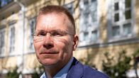 Silmälasipäinen mises katsoo kameraan keltaisen talon edustalla.
