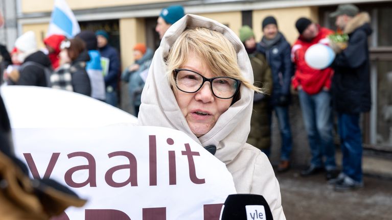Olga Jaroskaja haastateltavana. Pitelee valoista banderollia. Taustalla ihmisiä.