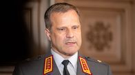 En man iklädd en grå kostym med rödgul brodering på kragen och guldiga symboler på axlarna.