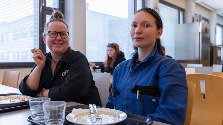 Hanna Saarinen ja Julia Häkkinen katsovat kameraan. He ovat pukeutuneet haalareihin. Pöydällä on kaksi tarjotinta, joissa on tyhjäksisyödyt lautaset.