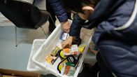 Käsiä kurottaa lattialla olevaan ruokalaatikkoon noukkimaan ruokapaketteja.