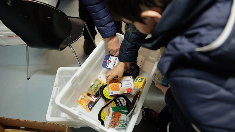 Hands reach into a large box of ready foods.