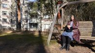 A woman sits in a wooden swing in an apartment block backyard. 
