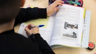 poika oppilas kirjoittaa oppikirjaan
