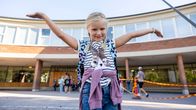 Ekaluokkalainen tyttö Sofia Voltti pitää käsiä levällään Meilahden ala-asteen pääoven edessä.