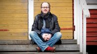 Kai Sadinmaa istuu Toimelan palstapuutarhan keskellä sijaitsevan rakennuksen portailla ja katsoo kameraan.