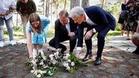 Kolme henkilöä asettelee kukkia maahan muistotilaisuudessa.
