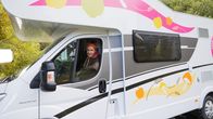 Mikko Kekäläinen asuntoauton ratissa. Auton kyljessä värikkäät tarrat, joissa omenoita ja sieniä.