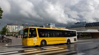 En gul stadsbuss kör på ett övergångsställe framför Centralstationen i Stockholm under molnig himmel.