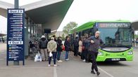 Människor stiger på en grön buss vid en stor busshållplats.