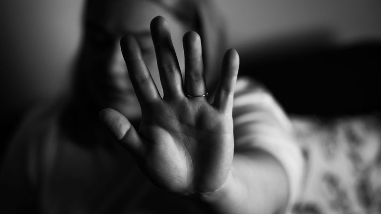 Murky black and white image of a woman holding her hand up to the camera in a defensive gesture.
