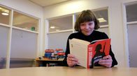 Nuori tyttö istuu pöydän ääressä katsoen kameraan, käsissään hänellä avattuna Väinö Linnan Sotaromaani.