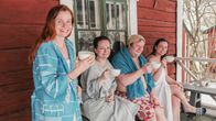 Kolme naista ja yksi mies vilvoittelevat kuistilla löylyjen jälkeen teekupit käsissään ja hymyilevät iloisesti.