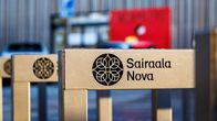 Polkupyöräteline sairaala Novan pihassa. Telineessä on sairaalan logo sekä nimi. Taustalla epätarkkana päivystyksen sisäänkäynti.