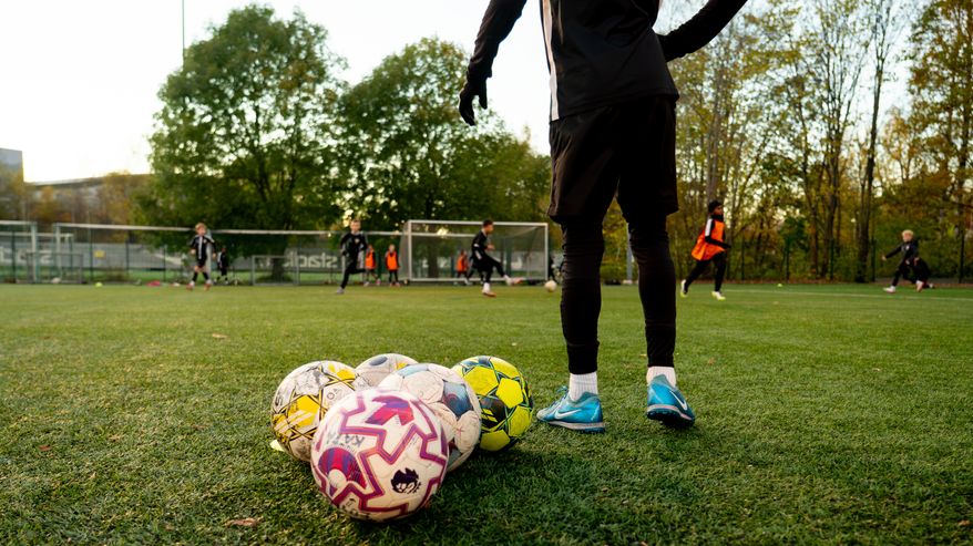 Barn spelar fotboll, i förgrunden syns fotbollar. 