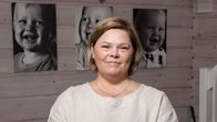 Nainen katsoo kameraan, taustalla valokuvia lapsista.