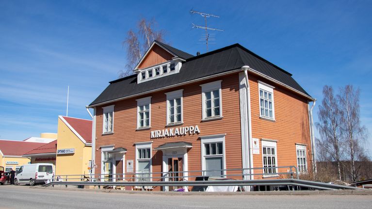 Vinhan kirjakauppa Ruoveden keskustassa. Kirjakaupan rakennus on puinen ja oranssi. Aurinko paistaa ja taivas on sininen.
