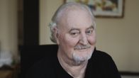 Neil Hardwick lähikuvassa katsoo suoraan kameraan, hymyilee hieman.