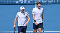 Kaksi tennispelaajaa kävelee kentällä mailat kädessä, taustalla verkko ja teksti “ATP TOUR”.