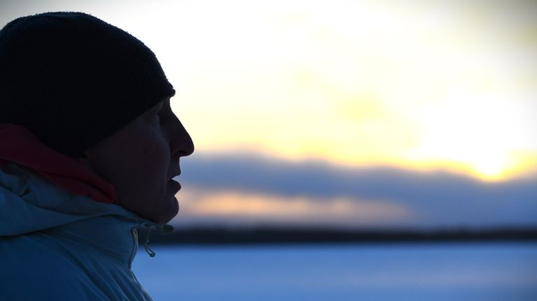 Orienteraren Mårten Boström i profil med vintrigt landskap vid solnedgång i bakgrunden.
