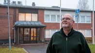 En man med skägg står framför en röd tegelbyggnad från 70-talet.
