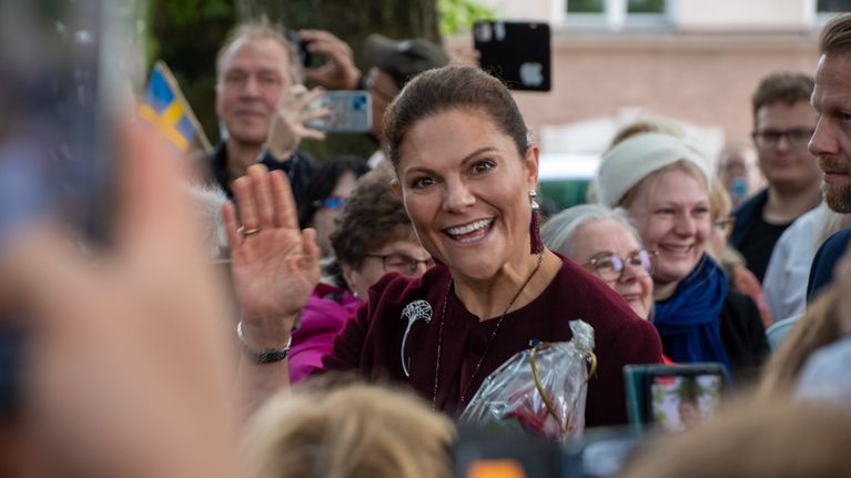 Kronprinsessan Victoria vinkar mot kameran. Hon befinner sig i en folkmassa.
