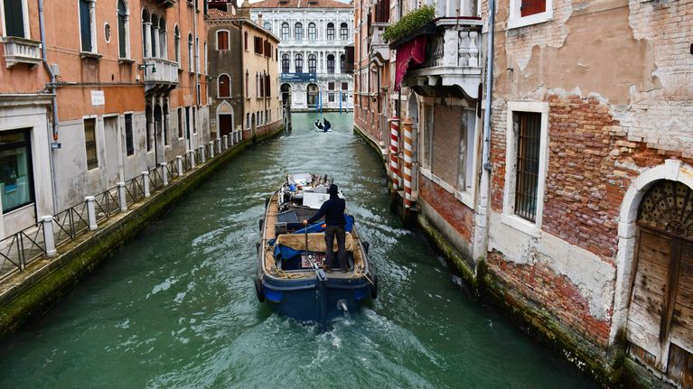 En båt i en kanal i Venedig, mellan två tegelstensbyggnader.