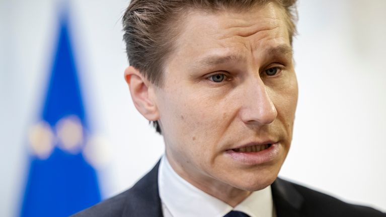 Tummatukkainen mies katsoo oikealle. Taustalla näkyy sininen EU-lippu.