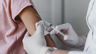 Ett barn får vaccin i armen av en person med vita plasthandskar och läkarrock på. 