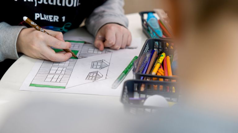 Oppilas värittää tussilla piirtämäänsä rakennusta paperille oppitunnilla.