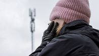 Nainen puhuu kännykkään, taustalla häämöttää matkapuhelinverkon tukiasema.