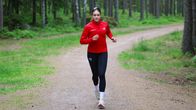 En person med röd skjorta på löper i en skog och tittar in i kameran.