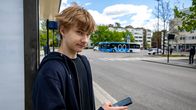 Photo shows a teenager at a bus stop.