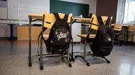 Kaksi reppua roikkuu tuolien selkänojissa tyhjässä luokkahuoneessa. 