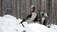 Soldater tränar i skogen under vinterförhållanden, klädda i kamouflage för snömiljöer och utrustade med vapen och kommunikationsutrustning.