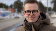 Mies ruskeassa takissa hymyilee.
