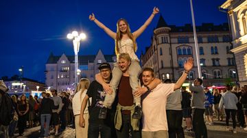 Nuori nainen on kiivennyt miehen olkapäille ja poseeraa nyt yhdessä muiden kavereiden kanssa tuulettaen kameralle.